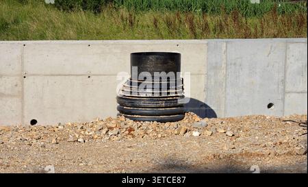 A vertical ribbed plastic manhole riser pipe emerges from a rocky ground surface next to a newly installed modular concrete barrier Stock Photo