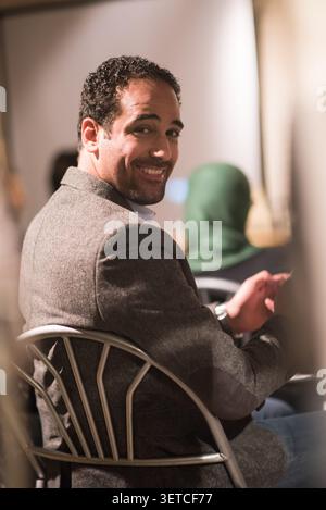 Authentic candid moment of young Middle Eastern professional man with warm smile turning toward camera during team meeting in modern bright office Stock Photo