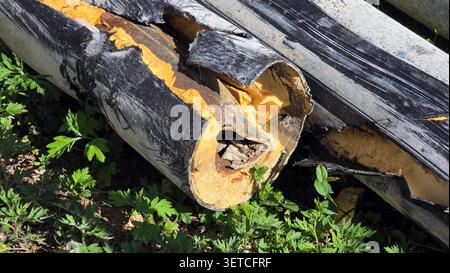 A damaged multi-layered district heating pipeline segment lies outdoors revealing a rusted inner carrier pipe thick orange thermal insulating foam Stock Photo