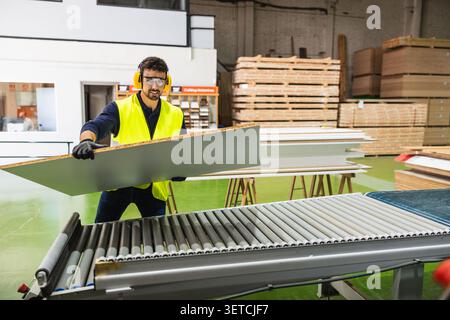 Worker operating machinery in a busy lumberyard warehouse Stock Photo