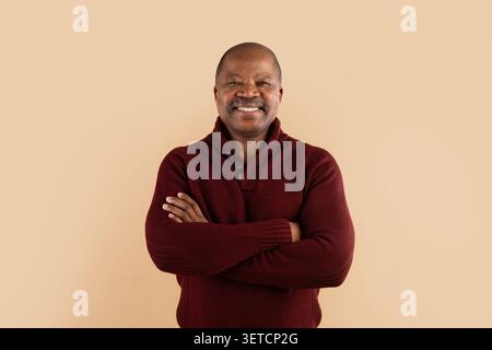 Smiling mature African American man in burgundy sweater standing with arms crossed Stock Photo