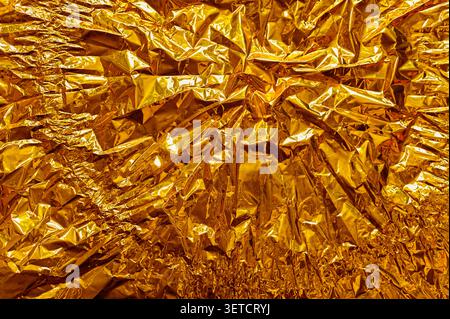 foil background with wrinkled golden material and glossy texture, foil creating complex folds and reflections, metallic abstract surface, vibrant tone Stock Photo