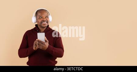 Mature African American man wearing wireless headphones and holding a smartphone Stock Photo