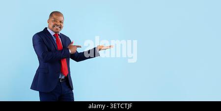 Smiling mature African American businessman in navy suit pointing at open palm Stock Photo