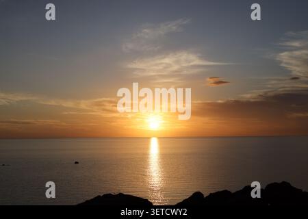 ocean sunset paints clouds white, gray, gold, orange, crimson at horizon (panorama, landscape, tropical, silhouette) Stock Photo