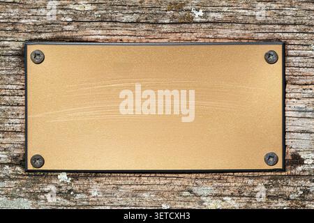 Brass plaque with a brush metal texture and screws attached and isolated on a wooden background, metal sign and signage stock photo image Stock Photo