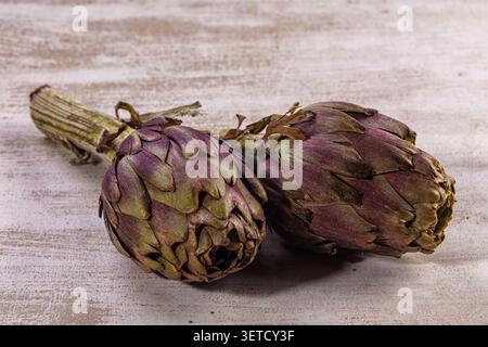 Two fresh purple green artichokes displayed on a rustic light wooden surface. Healthy, organic vegetable for cooking diet. Still life composition with Stock Photo