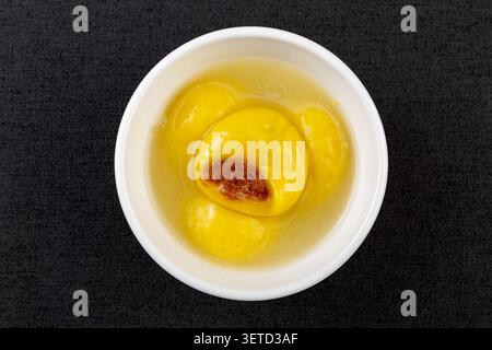 Yellow glutinous rice balls filled with brown sugar filling served in a traditional bowl on a wooden tray. Stock Photo