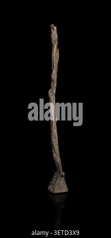 Minimalist bronze sculpture resembling a standing human figure by artist Lukas, photographed on a black background with reflection. Stock Photo