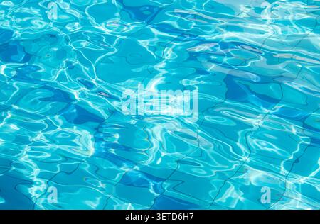 Side view of a blue-tiled outdoor swimming pool with crystal-clear water, shimmering and sparkling in the sun. Abstract water texture background. Stock Photo