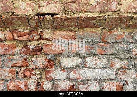 Close up of an old weathered brick wall with cracked plaster and exposed red bricks. Rustic grunge masonry texture background. Stock Photo