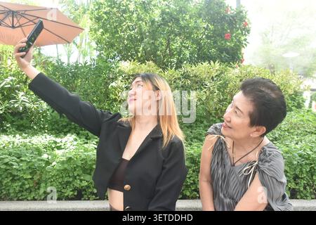 business woman and elder woman strong and healthy use mobile phone to selfie in community mall garden Stock Photo