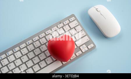 Red stress ball heart shape placed on computer keyboard next to wireless mouse on light blue desk representing healthcare technology online dating or Stock Photo