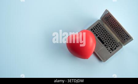 Top view of a toy laptop and a small red heart stress ball on a clean white background, symbolizing online dating, health technology, or corporate wel Stock Photo
