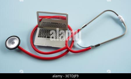 A miniature laptop computer placed inside the loop of a medical stethoscope tube, representing telemedicine, online healthcare, or digital medical rec Stock Photo