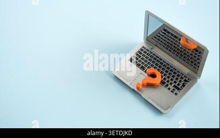 Miniature laptop computer with orange question mark on grey background Stock Photo