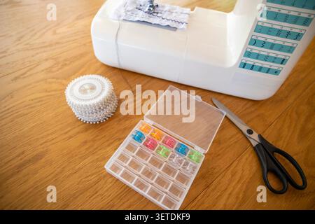 Sewing machine with bobbin box and scissors on wooden table, home sewing workspace. Concept: sewing organization Stock Photo
