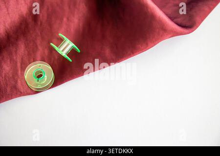 Sewing bobbins on burgundy fabric with copy space, textile crafting supplies. Concept: sewing materials Stock Photo