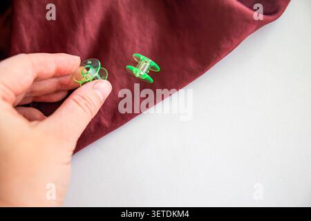 Hand holding sewing bobbin on burgundy fabric, textile crafting process. Concept: sewing workflow Stock Photo