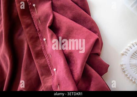 Burgundy fabric pinned for sewing on white background, textile preparation process. Concept: garment making Stock Photo