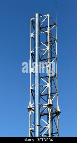 A tall stainless steel industrial chimney system secured by a metal truss support structure against a clear blue sky. Stock Photo