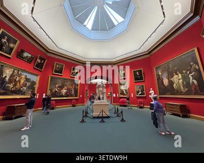 Visitors inside the National Galleries of Scotland, Edinburgh, observing classical oil paintings and a central marble sculpture beneath a dome. Stock Photo