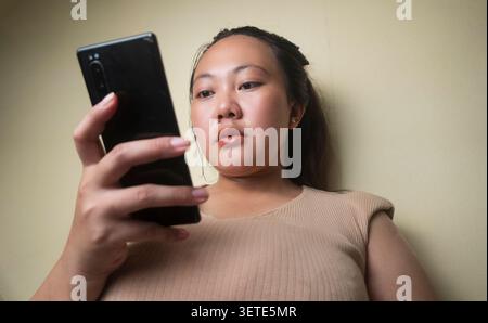 Young asian woman using a smartphone while looking at the screen indoors. Stock Photo