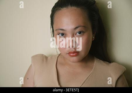 Serious young asian woman looking at the camera against a neutral indoor background. Stock Photo