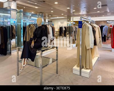 Clothing display in Harvey Nichols Edinburgh, featuring high-end apparel on hangers and a seated mannequin on a glass table. Stock Photo
