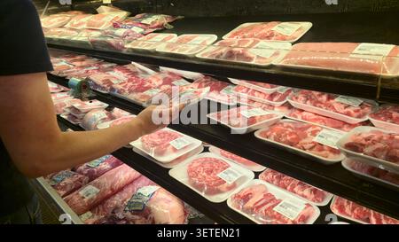 Shopper selects packaged fresh meat from refrigerated display in a supermarket Stock Photo