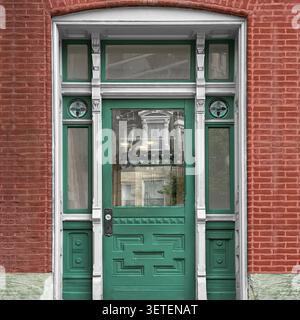 Green entrance door with decorative sidelights and transom on a red brick residential facade. Stock Photo