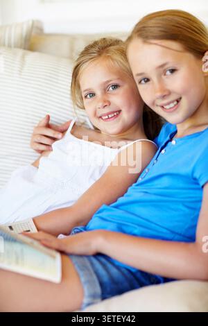 Bonding, portrait or children on sofa with book, literature hobby or reading in healthy relationship. Happy, siblings or sisters in home with hug Stock Photo