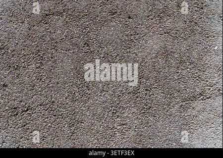 Exposed aggregate concrete texture background. Close-up view of a rough wall surface made of small pebbles, gravel, and cement. Stock Photo