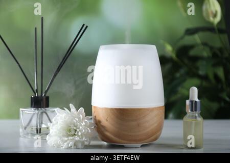 Aromatherapy. Aroma lamp, essential oil, reed diffuser and flower on white marble table outdoors Stock Photo