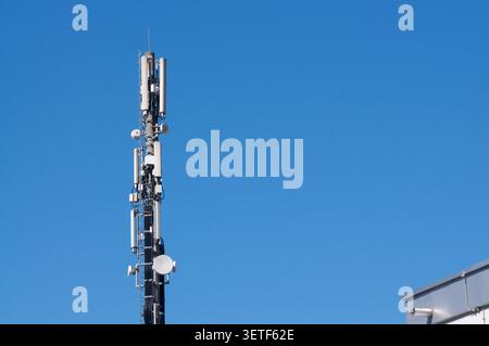 Low-angle view of a telecommunication tower mast equipped with 4G and 5G cellular antennas and microwave dishes against a clear blue sky. A conceptual Stock Photo