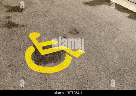 Top-down close-up view of the yellow disabled wheelchair parking icon printed on a rough, weathered grey asphalt street. A conceptual image focusing o Stock Photo