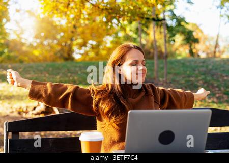 Happy woman enjoying remote work in autumn park. Work and life balance. Stock Photo