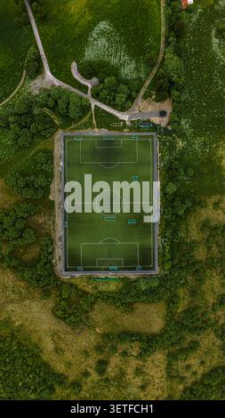 Aerial drone view of a pristine soccer field nestled in lush green forest landscape in Lofoten, Norway. The rectangular pitch with white Stock Photo