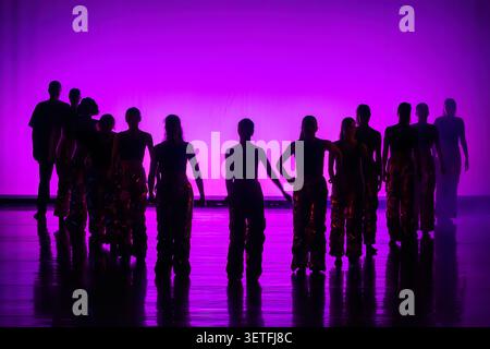 Dancers performing contemporary choreography in vibrant purple light Stock Photo