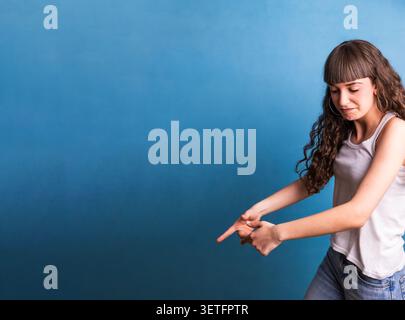Young woman pointing fingers down on blue background Stock Photo