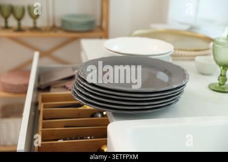Stack of clean grey plates on counter and cutlery in drawer indoors Stock Photo