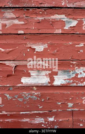 Red peeling paint coming off of wood slabs of a barn. Stock Photo