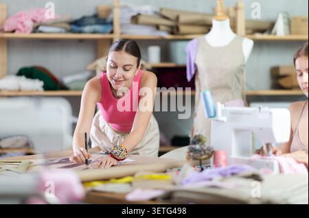 Female dressmakers working in the workshop against the background of racks with fabrics Stock Photo