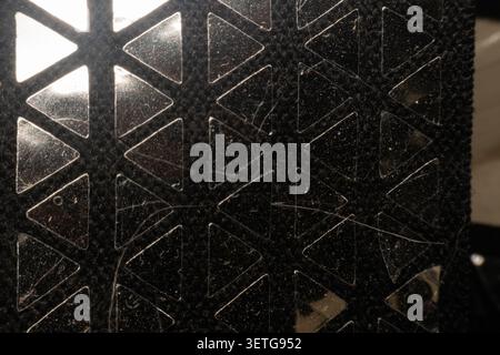 Closeup of a dusty geometric ventilation panel with triangular openings illuminated by backlight showcasing abstract texture pattern and industrial de Stock Photo