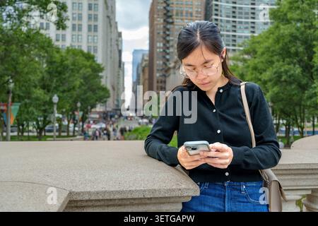 A young woman checks her smartphone while enjoying the cityscape of Chicago showcasing the fusion of technology and urban tourism. Stock Photo