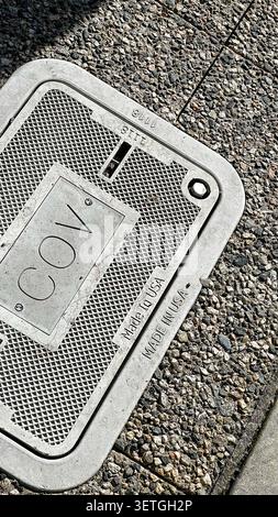 Vancouver, Canada - March 2, 2026: Metal City of Vancouver utility access cover stamped COV and Made in USA, its diamond mesh lid set into an aggregat Stock Photo