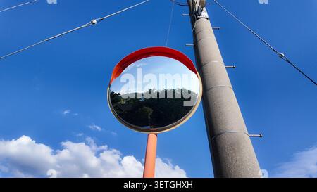 Low angle shot of a round traffic convex mirror next to a utility pole against blue sky. Stock Photo