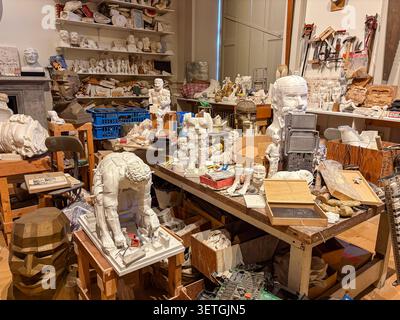 A workspace filled with various plaster sculptures, molds, and assorted hand tools on wooden tables and shelving units in a creative art studio. Stock Photo