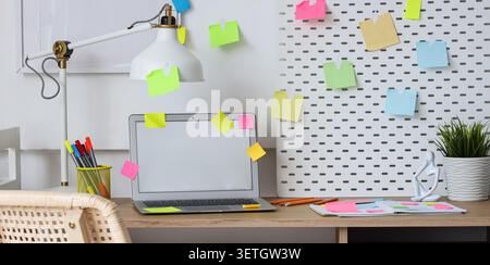 Organized workspace with laptop, sticky notes, and office supplies on desk Stock Photo