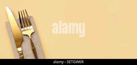 Golden knife and fork on beige napkin with yellow background Stock Photo